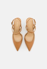 Scarpe con tacco alto in pelle color cuoio con design a punta, dotate di sottili cinturini e stile slingback, texture liscia e hardware in tonalità oro.