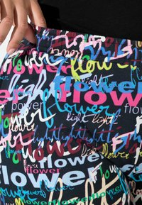 Multifarvede leggings med et mønster, der indeholder ord som "blomst" og "lys" i forskellige håndskrevne stilarter på en mørk baggrund.