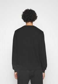 Sudadera negra de cuello redondo con mangas largas, hecha de una tela suave. Presenta un dobladillo y puños acanalados, diseño minimalista, sin logotipos visibles.