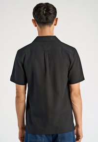 Camicia nera a maniche corte con una vestibilità rilassata, caratterizzata da una piega sul retro, colletto a viso e un tessuto liscio e testurizzato.