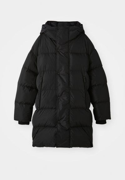 Manteau noir en duvet avec capuche, présentant un design matelassé, des fermetures à pression, des poches zippées et des poignets côtelés. Fabriqué en matériau brillant et lisse.