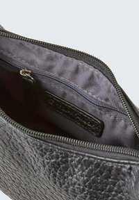 Interno di una borsa in pelle nera con una tasca con zip, esterno strutturato e fodera liscia. Presenta un'etichetta con marchio all'interno.