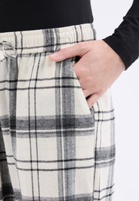 Pantalones de pijama a cuadros en beige y negro de franela, con cintura elástica y bolsillos laterales. La textura suave mejora la comodidad.