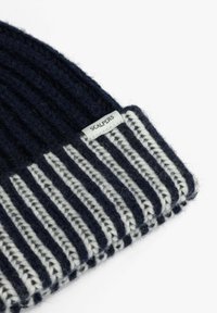 Gorro de punto acanalado en azul marino y blanco con un puño doblado y una pequeña etiqueta de la marca "Scalpers" en el puño.
