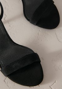 Sandalias negras de tacón alto con parte superior de imitación de piel de serpiente texturizada y una suave correa de ante en la parte del dedo del pie, que presenta un diseño de punta afilada.