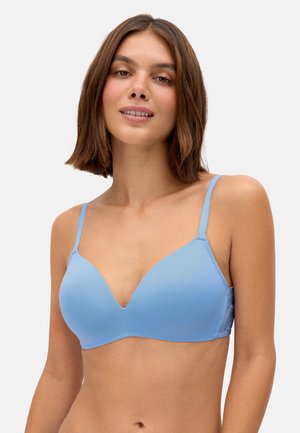 Joven con cabello castaño hasta los hombros que lleva un sujetador azul claro sin costuras, ligeramente acolchado, con tirantes finos ajustables.