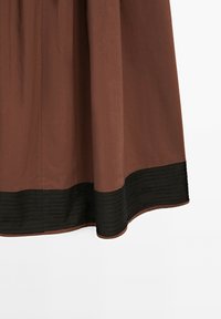 Brown cotton skirt with a black ribbed hem. The fabric has a smooth texture, and the design features a simple, flowing silhouette.