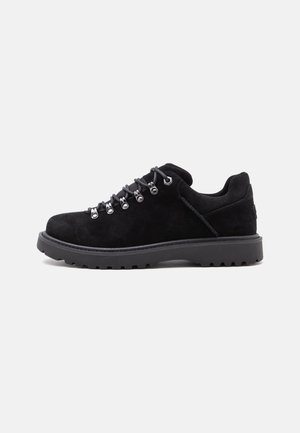 Chaussure de randonnée en daim noir avec semelle épaisse en caoutchouc et œillets métalliques, lacée avec des lacets gris sur fond blanc.