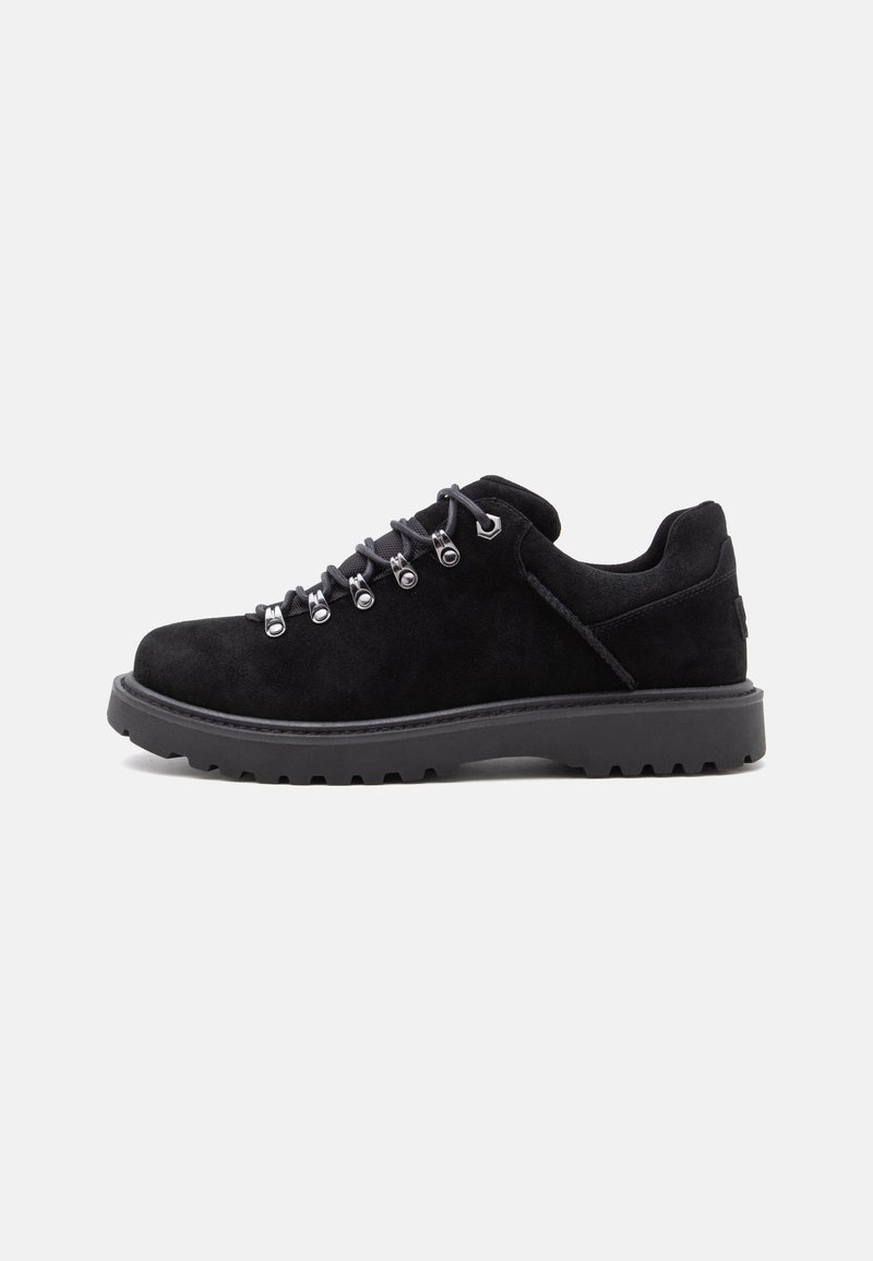 Chaussure de randonnée en daim noir avec semelle épaisse en caoutchouc et œillets métalliques, lacée avec des lacets gris sur fond blanc.