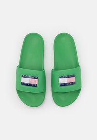 Chanclas verdes con un acabado suave y brillante. Presentan un parche rectangular de logo azul en la correa, con acentos en blanco, rosa y azul marino.