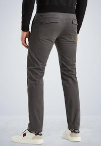 Grau melierte Baumwollhose mit schmaler Passform, ausgestattet mit zwei Gesäßtaschen und subtilen Steppnähten, kombiniert mit weißen Sneakers.