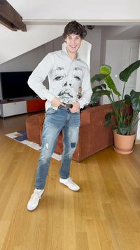 Marškiniai su juodai baltais dryžiais, puoštas veido atspaudu, derinami su nusidėvėjusiais mėlynais džinsais ir baltais sportbačiais. Vidaus erdvė su augalais.