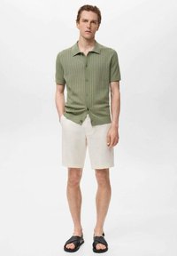 Camisa verde de manga corta con textura acanalada y botones, combinada con pantalones cortos beige claros y sandalias de slide negras. Un look simple y casual con una textura sutil.