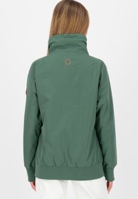 Grøn, letvægtsjakke med høj krave, elastiske manchetter og kant. Har et lille logo på ryggen og en glat, mat overflade.