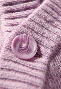 Helles lila gestricktes Gewebe mit einem strukturierten Muster, versehen mit einem glänzenden, runden Knopf in passender Farbe zum Stoff, mit vier Knopflöchern.