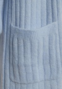 Světle modrá, žebrovaná pletenina s měkkou texturou má obdélníkovou přední kapsu. Design je jednoduchý a nezdobený.