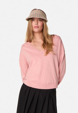 Pull rose en v avec un ourlet côtelé et des détails en forme de coquille, assorti à une casquette à motifs. La tenue présente des manches décontractées et une coupe loose.