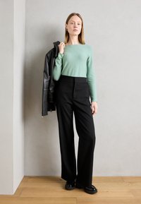Világoszöld, hosszú ujjú felső, amelyet magas derekú, fekete, bő szárú nadrággal viselnek. A modell egy fekete bőrkabátot tart a vállán.