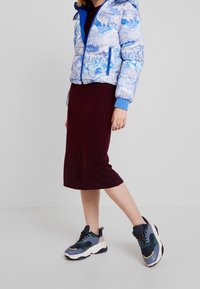 Puffer-takki sinisellä vuoristokuvioinnilla ja sinisillä yksityiskohdilla, yhdistetty burgundinväriseen polvitiehen hameeseen ja monivärisiin paksupohjaisiin lenkkareihin.