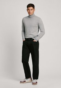 Grijze coltrui, zwarte broek en witte sneakers met rode accenten. Stof lijkt glad; de broek zit losjes. Merkenlabel zichtbaar.