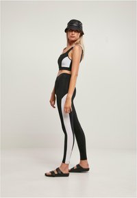 Čiernobiely set športového oblečenia pozostávajúci z crop topu s vzorovaným dizajnom a vysokými legínami s kontrastnými bočnými panelmi.