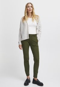 Svetlo siva jopica z gumbi, bela oprijeta majica in temno zelene slim-fit hlače. Črne masivne loafers čevlje dopolnjujejo outfit.