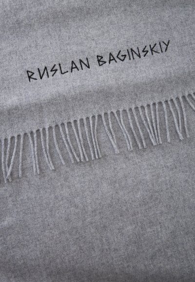 Tissu gris clair avec bord effiloché et texte noir brodé « "RUSLAN BAGINSKIY" » incliné sur le tissu.