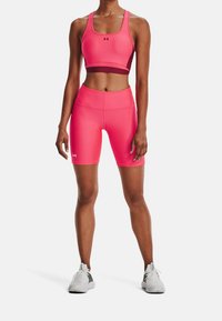 Różowy stanik sportowy i pasujące szorty wykonane z elastycznego materiału, posiadające dopasowany krój i akcenty z logo. Uzupełnione białymi butami sportowymi.