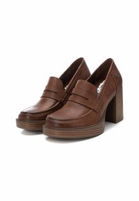 Mocasines de tacón de cuero marrón con punta redonda, detalle de correa decorativa y un tacón texturizado y grueso. Presentan un acabado suave y pulido.