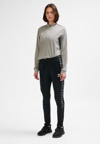 Grå långärmad tröja med dragkedja och svarta detaljer, kombinerad med svarta träningsbyxor med fiskbensmönster längs sidorna. Svarta sneakers.