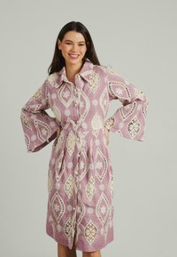 Vestito rosa con motivi in pizzo floreale, chiusura frontale con bottoni e maniche a campana. Tessuto testurizzato con vita aderente e gonna svasata.