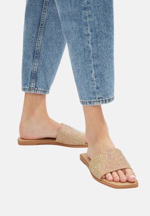 Flache Riemchensandalen mit einem beigen Riemen, der mit mehrfarbigen Strasssteinen verziert ist, ausgestattet mit einer flexiblen Sohle und glatter Textur.