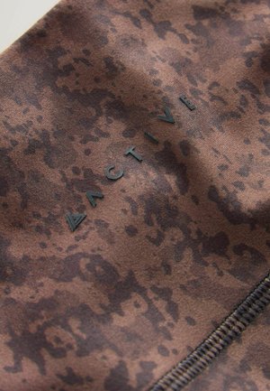 Brauner Stoff mit einem marmorierten Muster, das das Wort "ACTIVE" in schwarzer Schrift und eine sichtbare Nahtdetail aufweist.