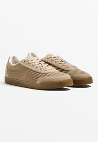 Beige sportcipők, hálós felsőrésszel, velúr részletekkel, párnázott nyakkal és texturált felületű gumitalppal. Fűzős kialakítás.