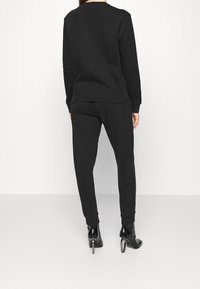 Svart sweatshirt och matchande sweatpants, båda i ett mjukt tyg. Byxorna har slim fit och avslut, med svarta högklackade stövlar.