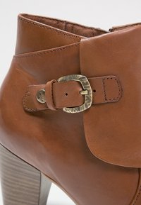 Bottine en cuir marron avec talon bloc et détail de bride à boucle en laiton sur le côté.