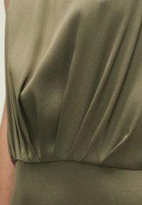 Robe vert olive en tissu doux et texturé, avec des détails plissés autour de l'encolure et une silhouette lisse et ajustée à la taille.