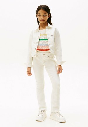 Veste en denim blanche sur un pull à motifs multicolores, assortie à un jean skinny blanc et des baskets blanches. Design simple et couleurs neutres.