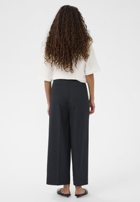 Mørke vidde bukser med glat tekstur, høj talje og diskrete sømdetaljer bagpå. Kombineret med en løs hvid top.