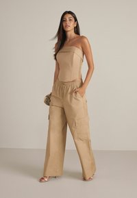 Beige strapless topp med en strukturerad bodice och sidofållningar, kombinerat med vida beige cargobyxor med resårmidja och fickor.