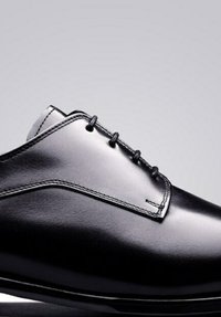 Zwarte leren nette schoen met een gladde textuur, spitse neus en zes veterogen. Heeft subtiele stiksels langs de zijkanten en een glanzende afwerking.