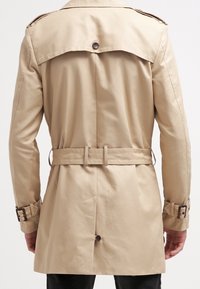Béžový trenčkot s dvojřadým zapínáním, páskem v pase, knoflíkovými doplňky a ramenními nášivkami. Hladká, lehká látka.