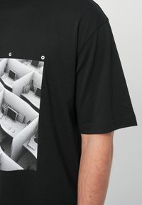 Μαύρο βαμβακερό μπλουζάκι με μονόχρωμο γραφικό από γραφειακές καμπίνες με υπολογιστές, κοντά μανίκια και άνετη εφαρμογή.