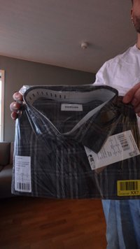 Camicia a maniche corte a quadri neri e grigi in confezione di plastica, con colletto, etichette attaccate e un'etichetta con informazioni sulla taglia.