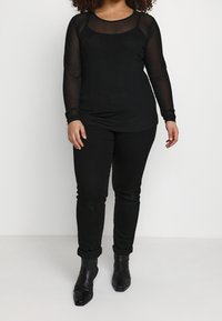 Haut noir en mesh à manches longues avec un col rond et un motif à pois, associé à un pantalon noir ajusté et des bottines à bout pointu.