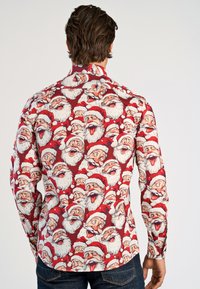 Langsleevhemd, rode stof met een herhalend patroon van lachende Santa-gezichten, gedetailleerd met witte baarden en rode hoeden.