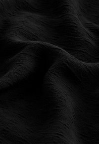 Tissu noir texturé qui tombe avec des plis visibles, montrant une surface douce et légèrement inégale. Le matériau semble léger et délicat.