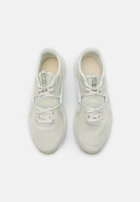 Light gray mesh athletic shoes with a textured surface, featuring a padded collar, lace-up design, and neon accents on the logo and sole.