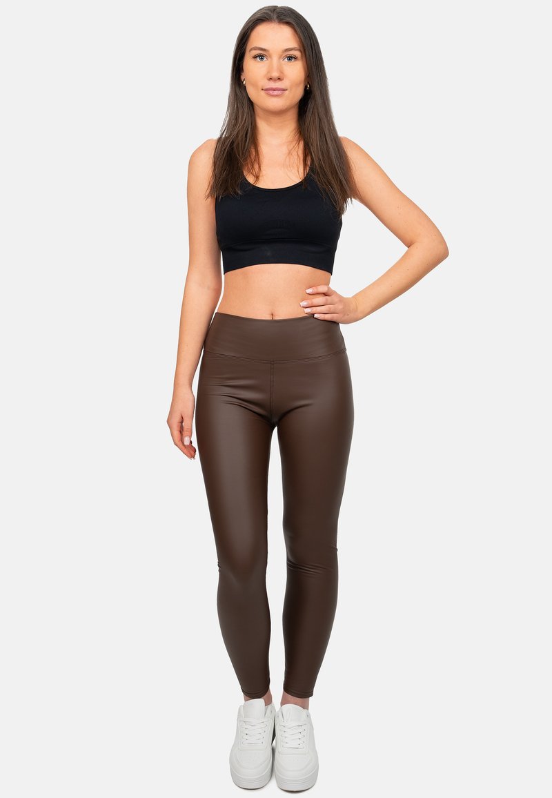 Leggings in finta pelle marrone con vita alta, abbinati a un crop top nero e sneaker bianche. Texture liscia e design aderente.