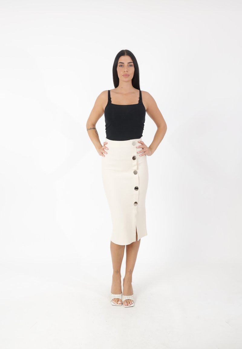 Schwarzes, tailliertes Tanktop, cremiger Midirock mit Knopfdetails vorne und einem Schlitz, getragen mit weißen, sensationellen Sandalen. Glatte Stoffstruktur.